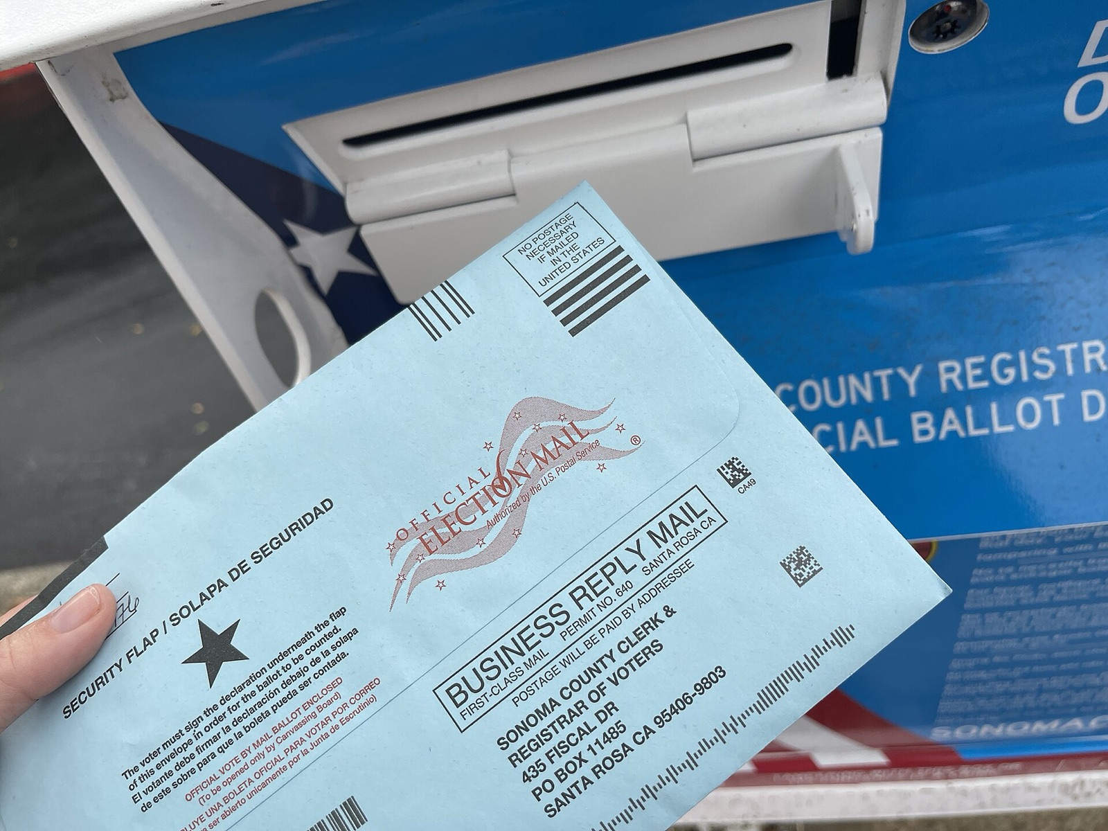Real United States mail ballot beside an official ballot drop box