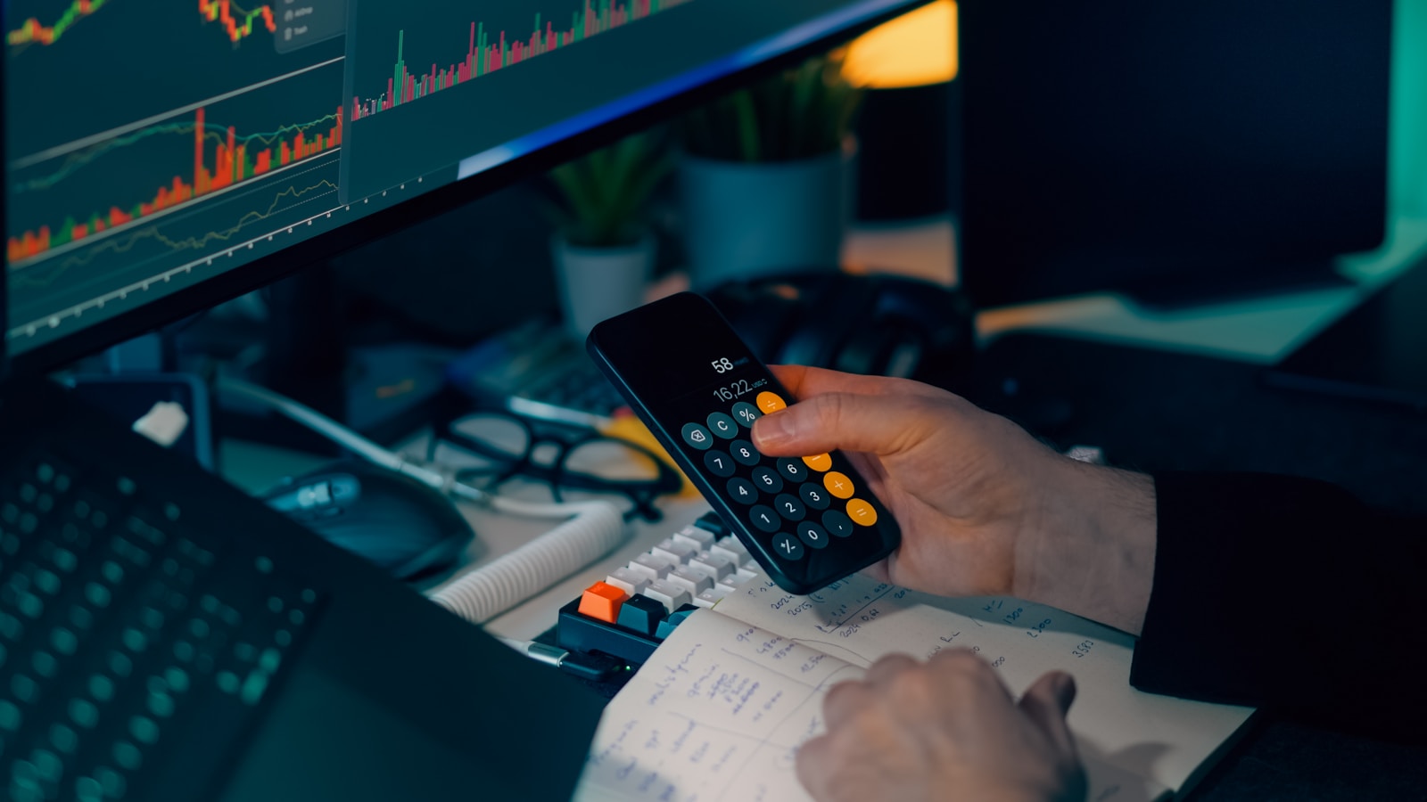 Person calculating risk beside financial charts at a trading desk